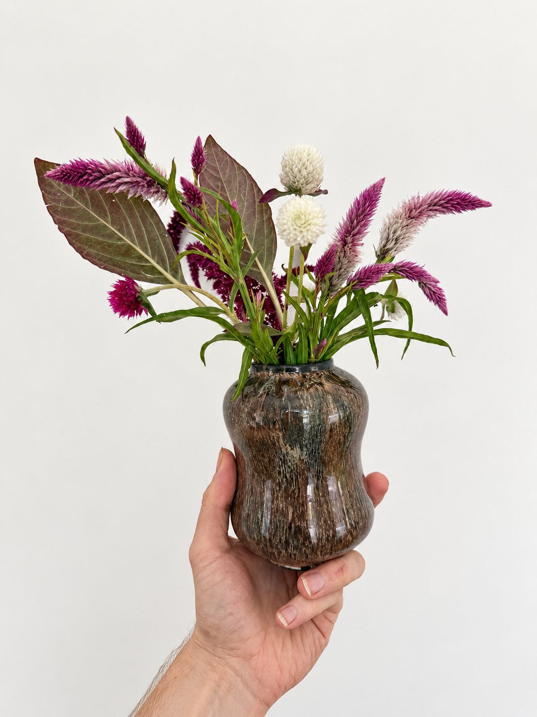 Pink celosia and white gomphrena in a mottled brown hourglass vase