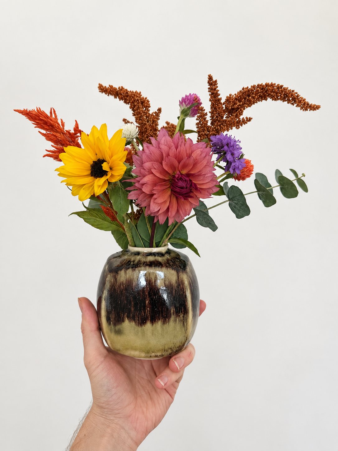 Dahlia, sunflower, amaranth and eucalyptus in an olive vase with a dark tenmoku band