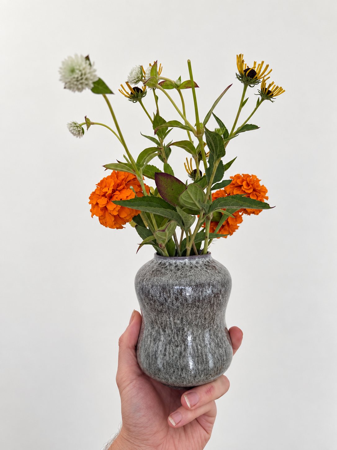 Marigolds, gomphrena and black-eyed susans in a speckled grey hourglass vase