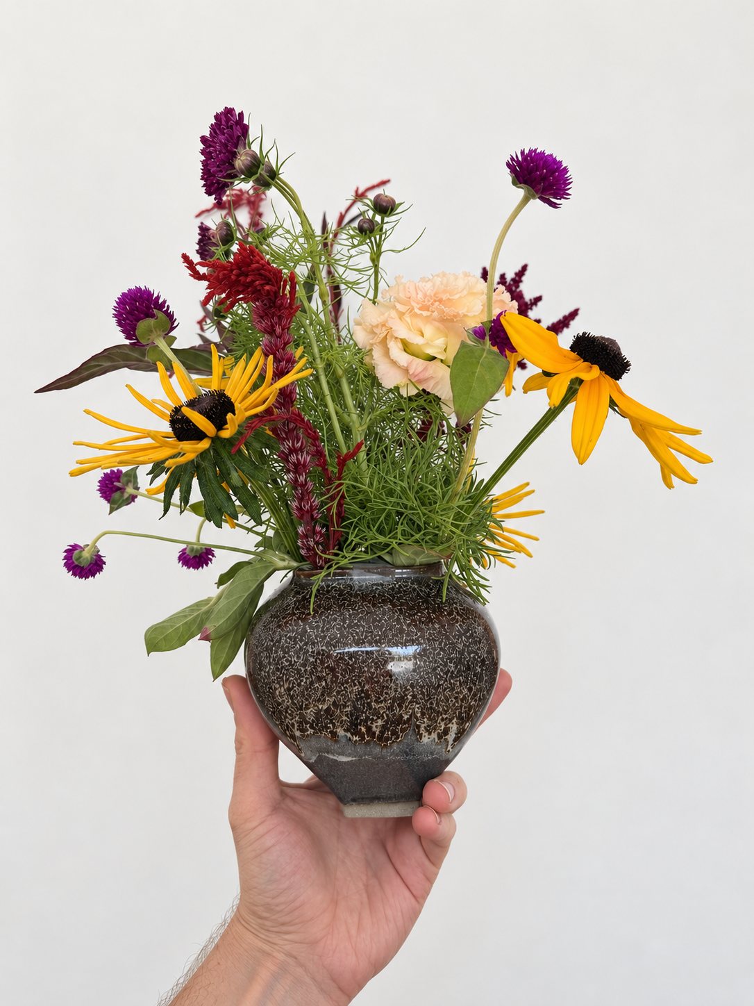 Rudbeckia, gomphrena, celosia and cosmos foliage in a dark speckled round vase