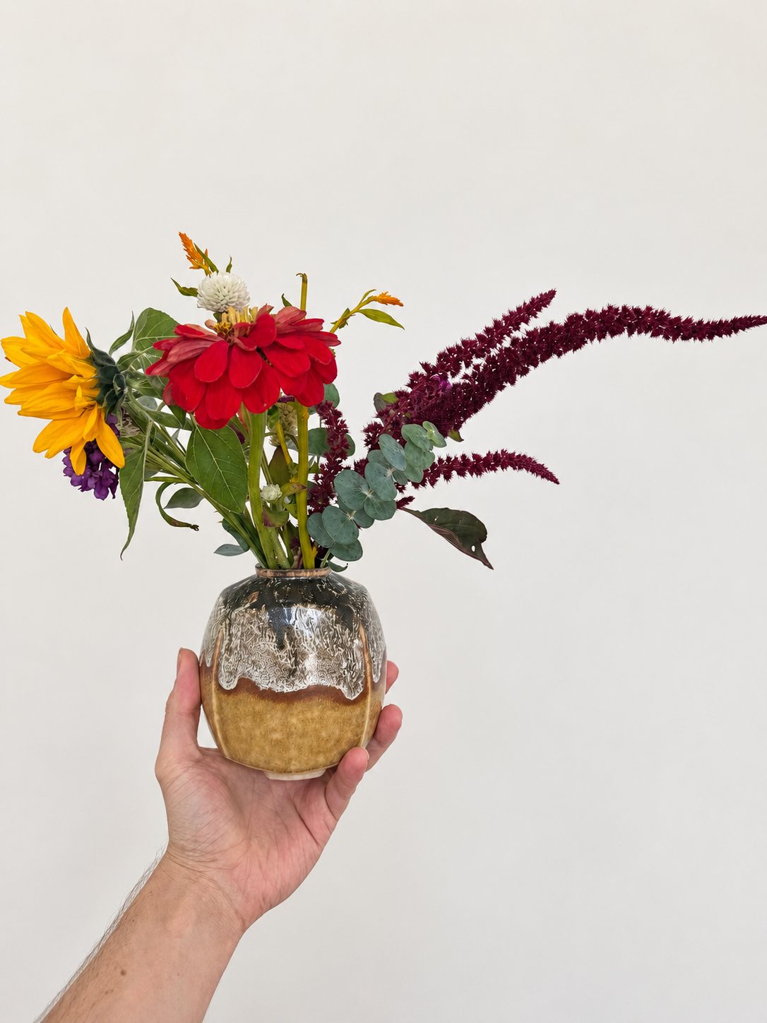 Red zinnia, sunflower and trailing amaranth in an amber vase with a white drip